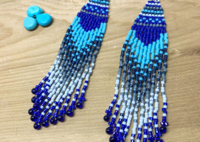 Wave of Blue Fringe Ombre Woven earrings on wood background.